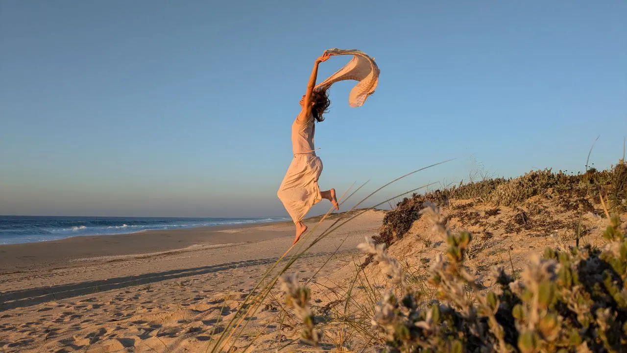 Susanne leaping on the beach with a scarf flying in the wind
