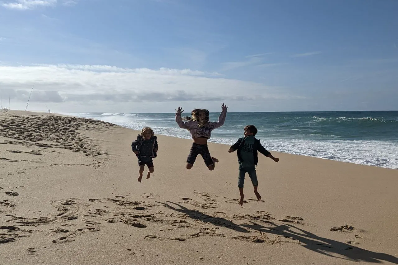 Three children jumping for joy on a wide sandy beach by the ocean