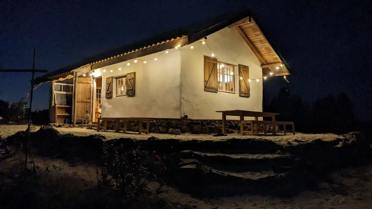 The white clay community house at night, lit up with a string of warm lights