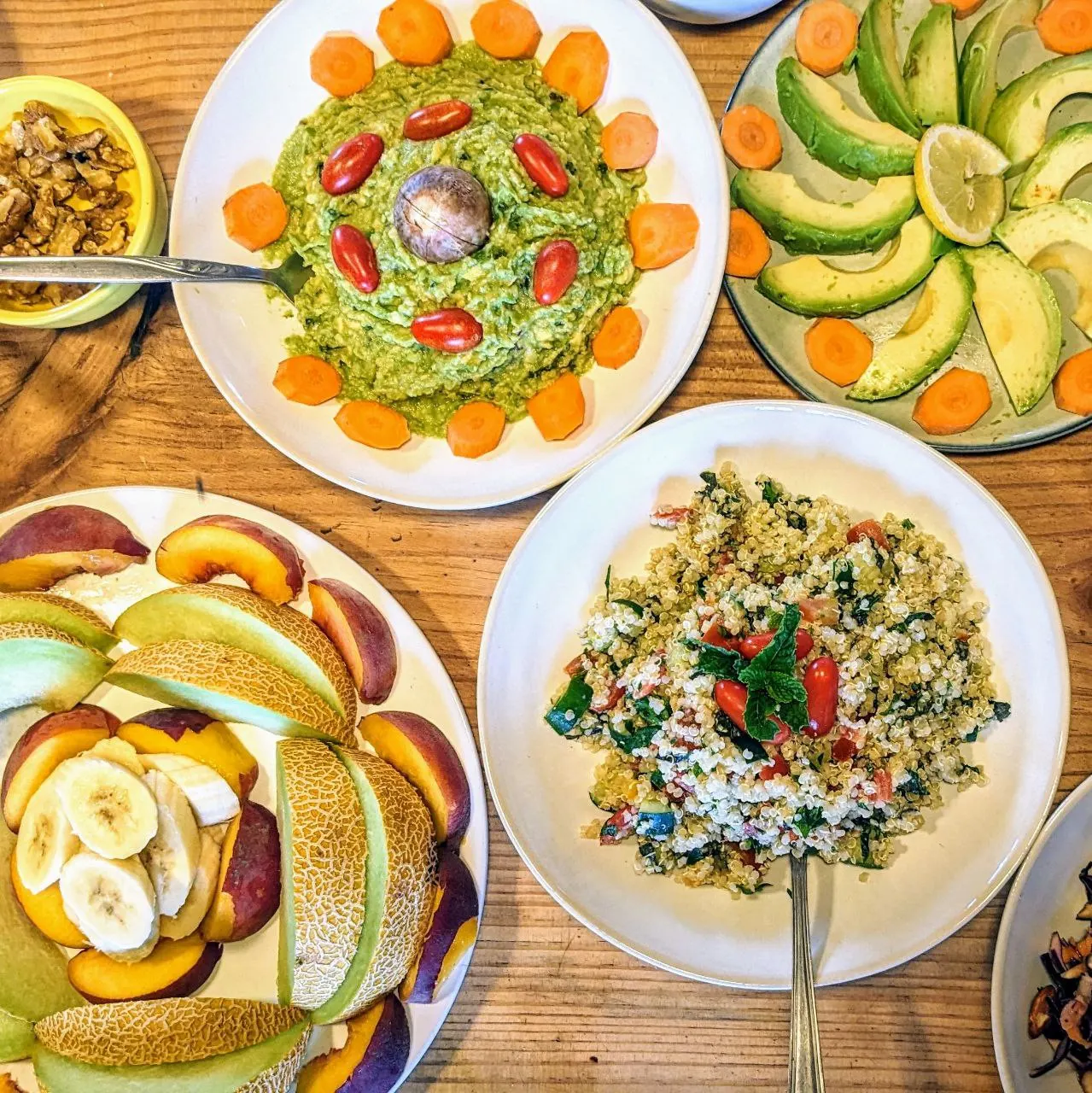 Plates of colourful vegan food on a wooden table: guacamole, avocado, quinoa salad and fresh fruit