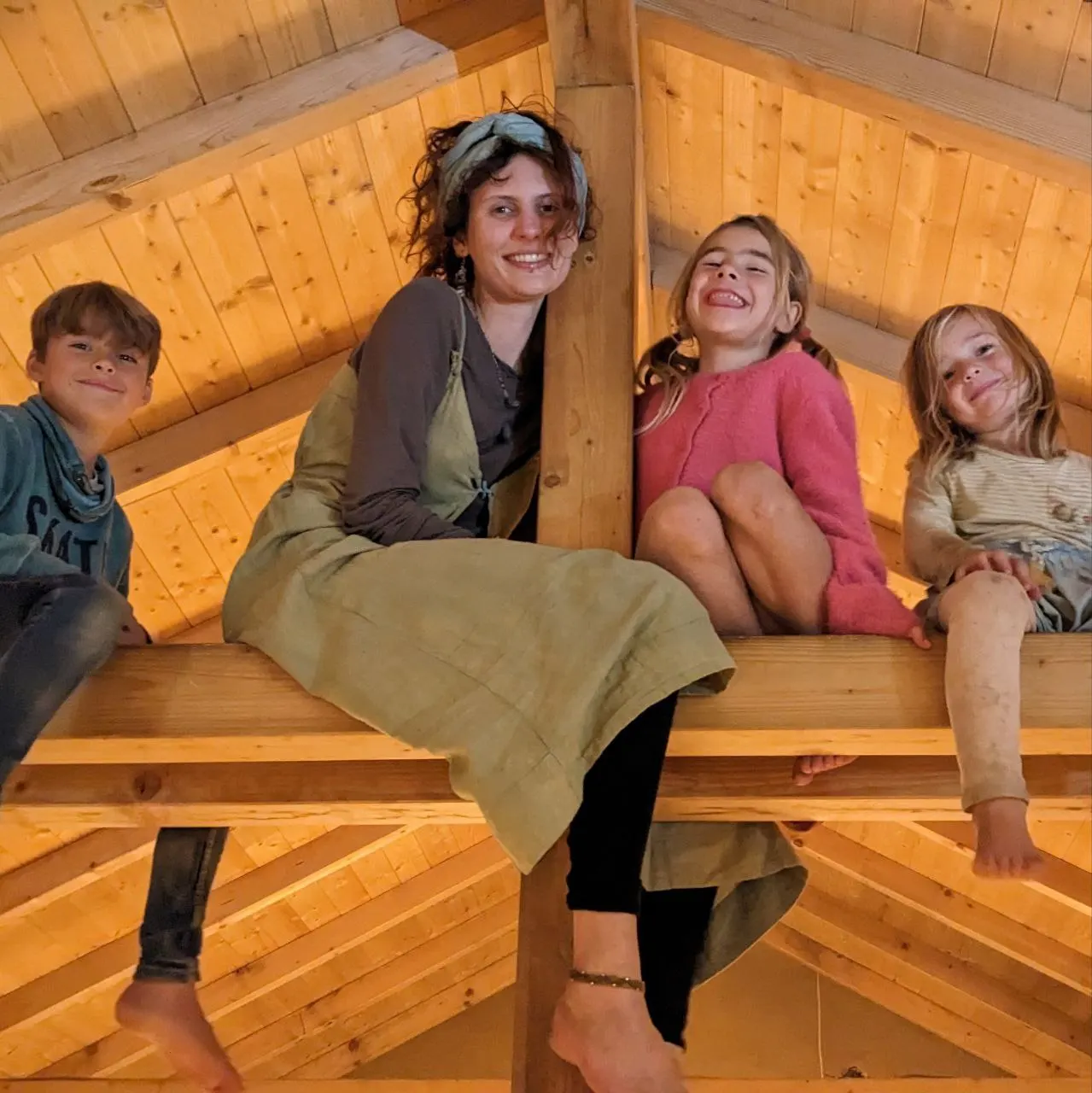 Children and an adult smiling together in a wooden loft at Malama