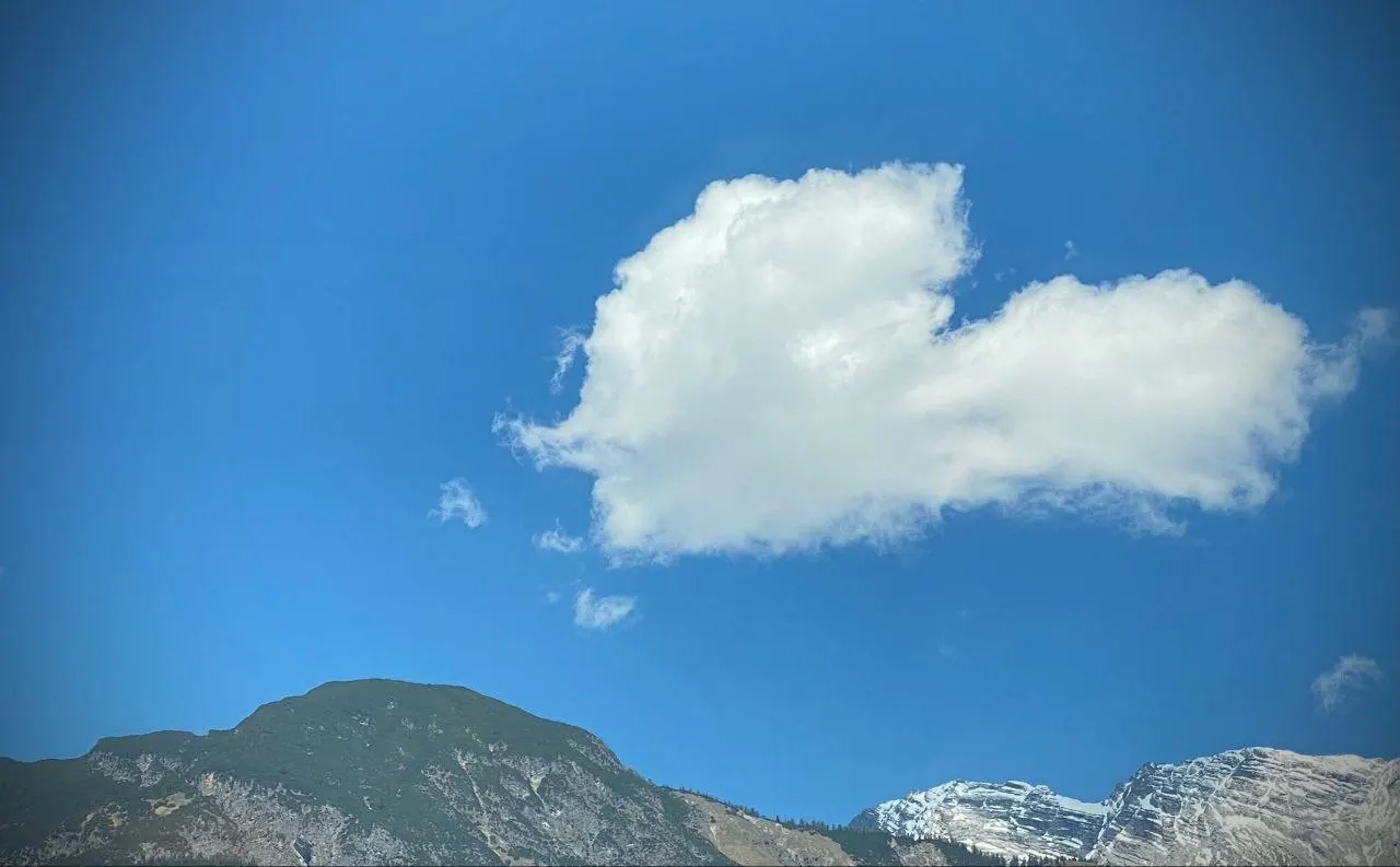 A heart-shaped cloud in a blue sky above mountains