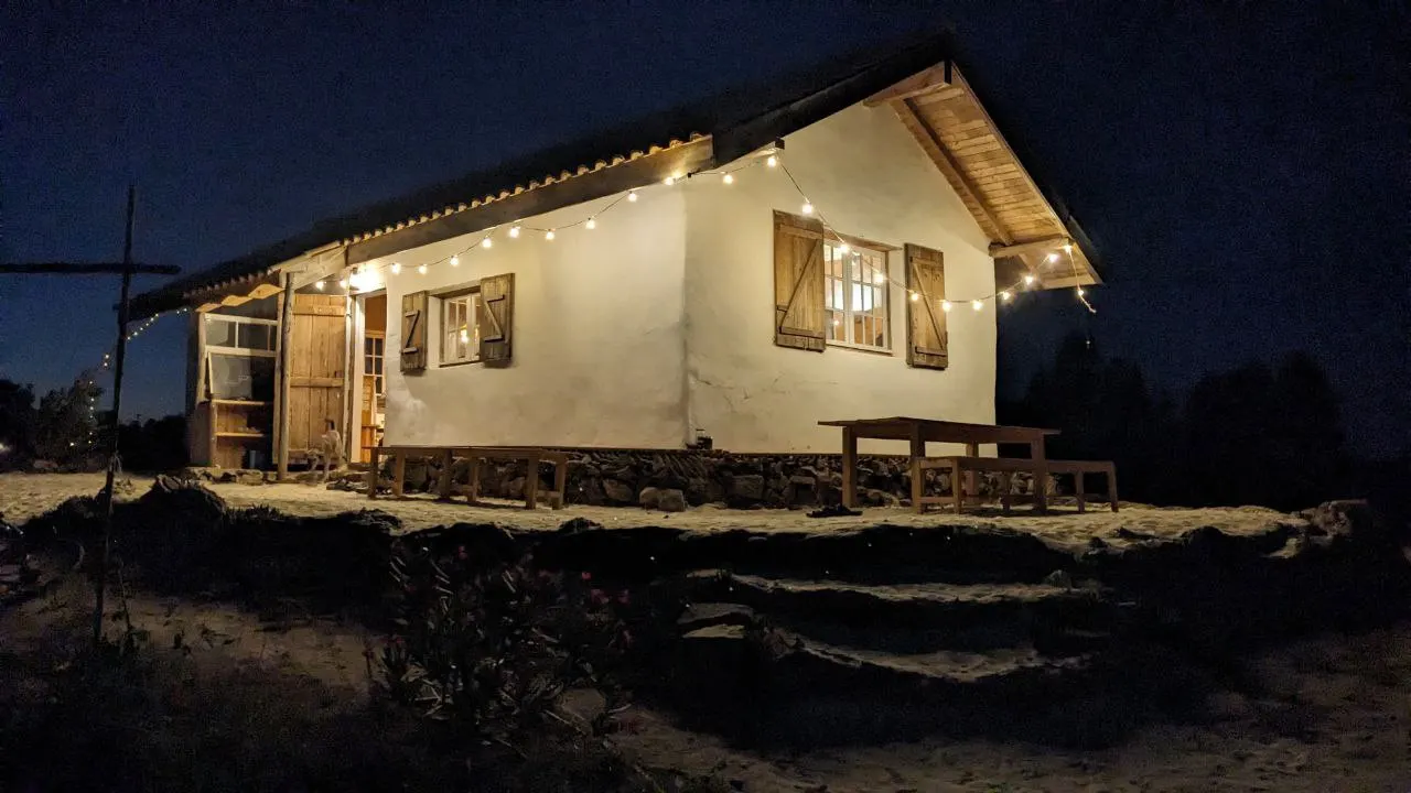 The white clay community house at night, lit up with a string of warm lights